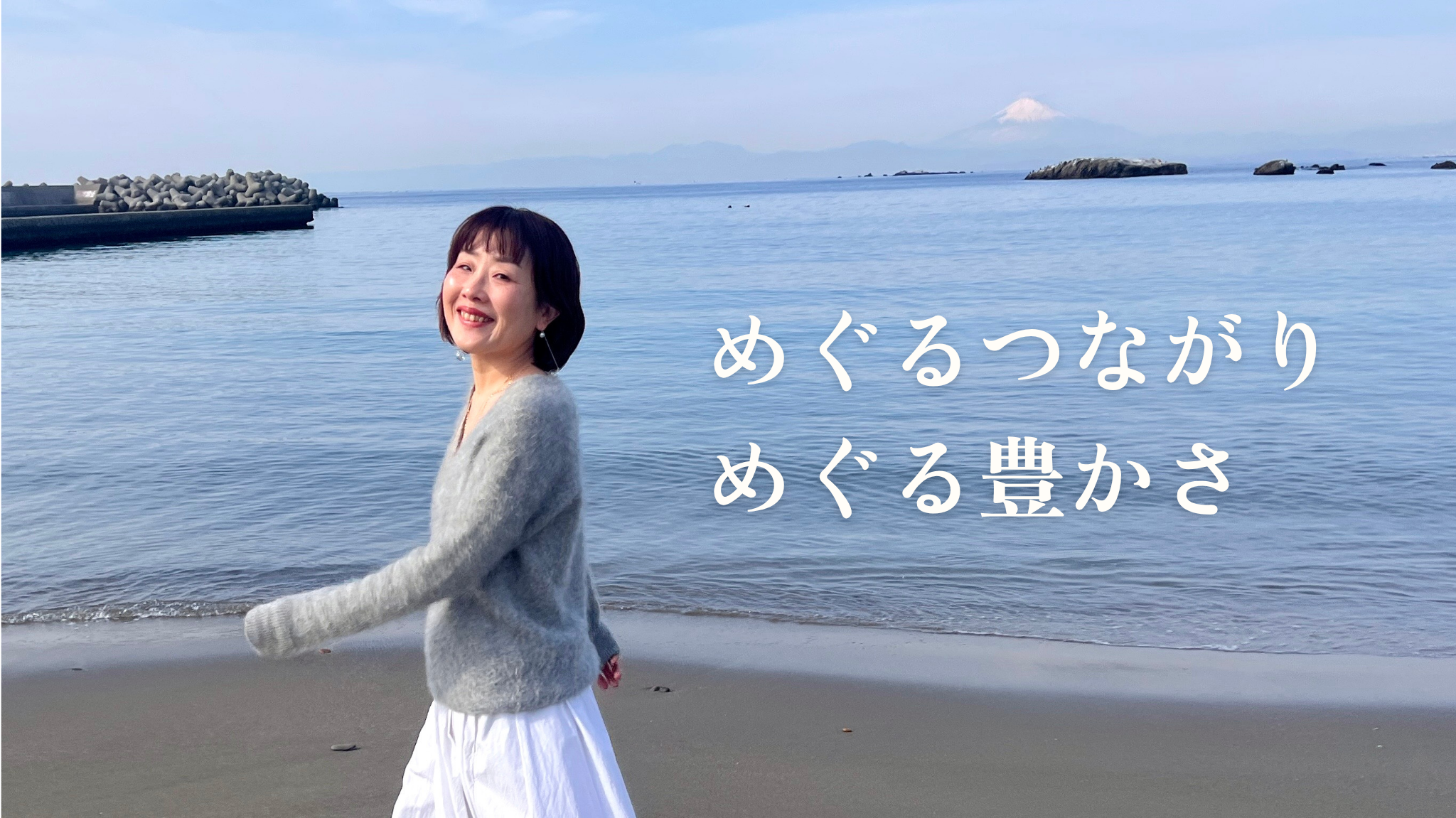 海で歩きながら微笑む友里「めぐる繋がり　めぐる豊かさ」のメッセージ